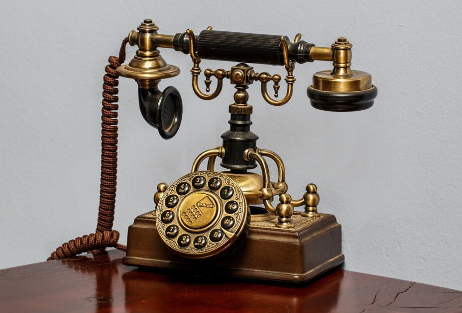 Altes Metalltelefon mit Wählscheibe in warmem Rotgold, der Hörer ruht auf einer geschwungenen Ablage.